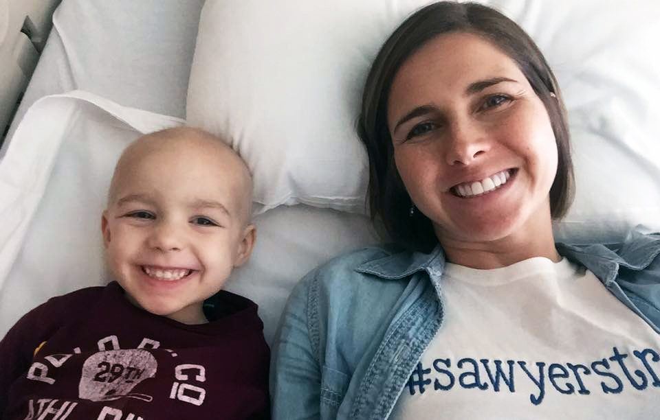 在她的儿子索耶接受癌症治疗期间，儿科癌症护理人员阿曼达·哈克站在他旁边