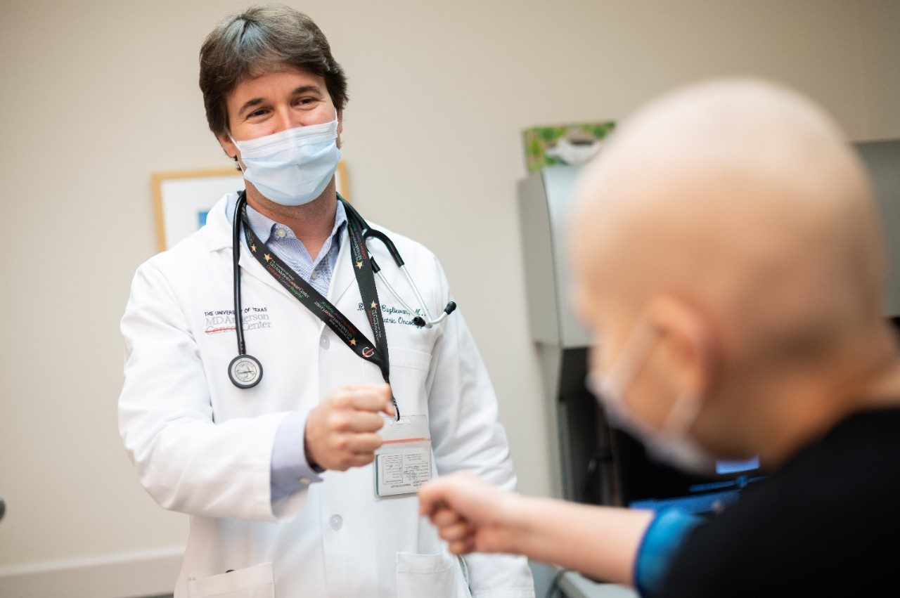 Branko CuglievanMD穿白大衣时,在诊所戴医疗级面罩时与一位小儿白血病病人握起拳头
