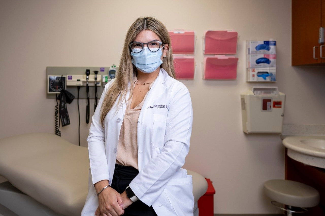 Latinx护士阿什利·马丁内斯和她的手坐在房间里一间诊所的文件夹挂在她身后的背景。