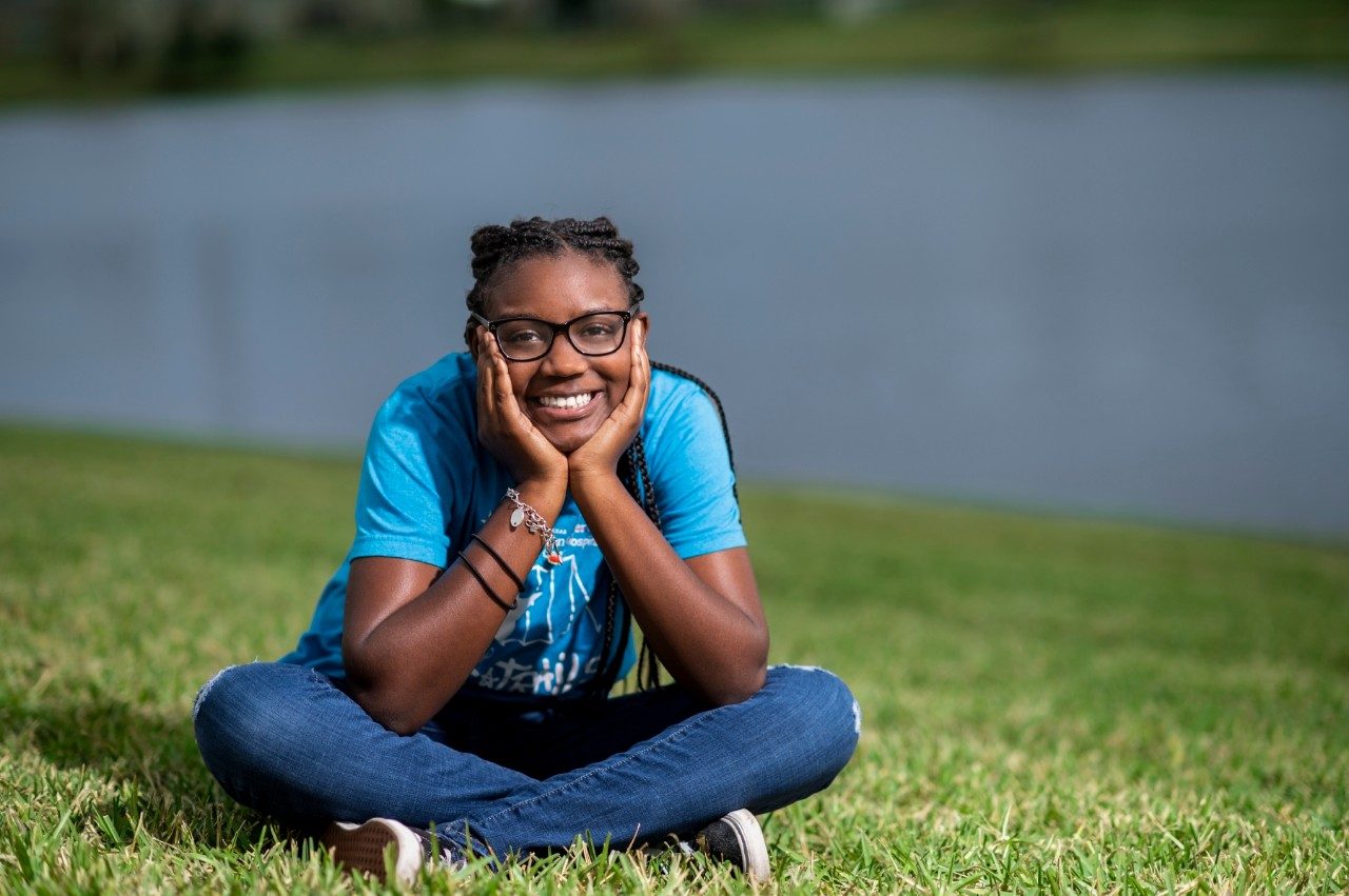 幼年白血病幸存者Akilah Lopez手伸下巴坐在草坪上