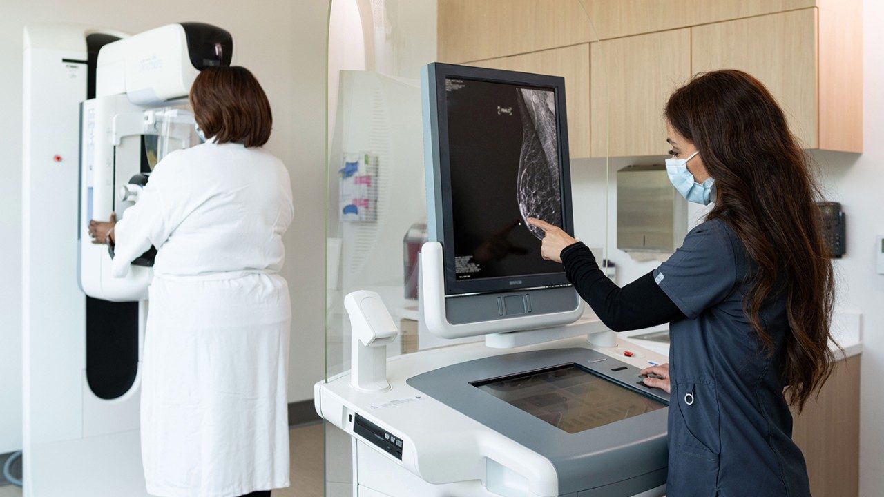 一个人在一件白袍面临乳房x光机MD安德森林地而拉丁乳房x光技师检查乳房的数字图像在屏幕上。